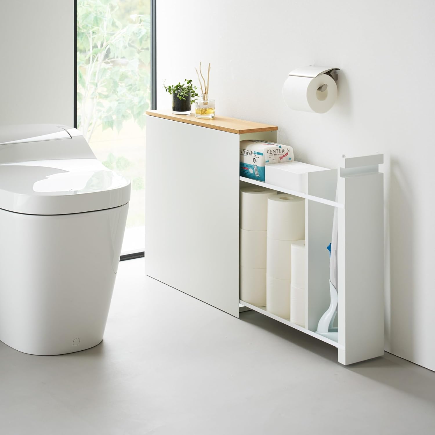 Slim white pull-out bathroom cabinet with wood top storing toilet paper and cleaning supplies